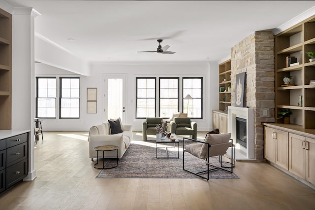 living room featuring built in shelves, a large fireplace, a healthy amount of sunlight, and light wood-style flooring