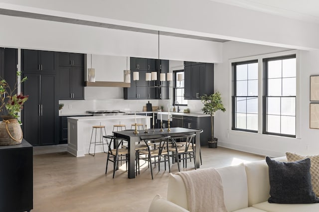 kitchen with light wood finished floors, light countertops, backsplash, wall chimney range hood, and dark cabinetry