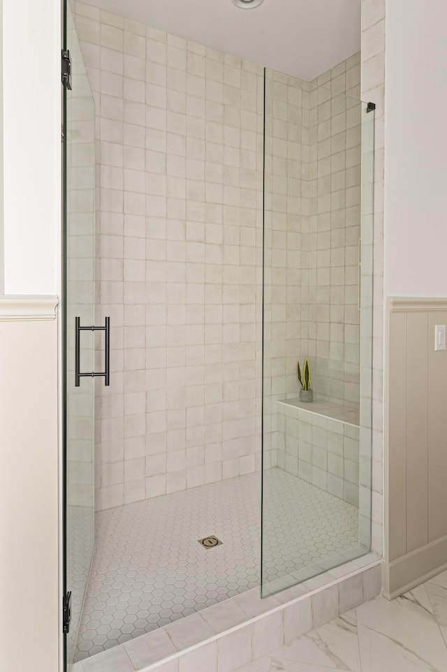 full bath featuring marble finish floor, a shower stall, and a wainscoted wall