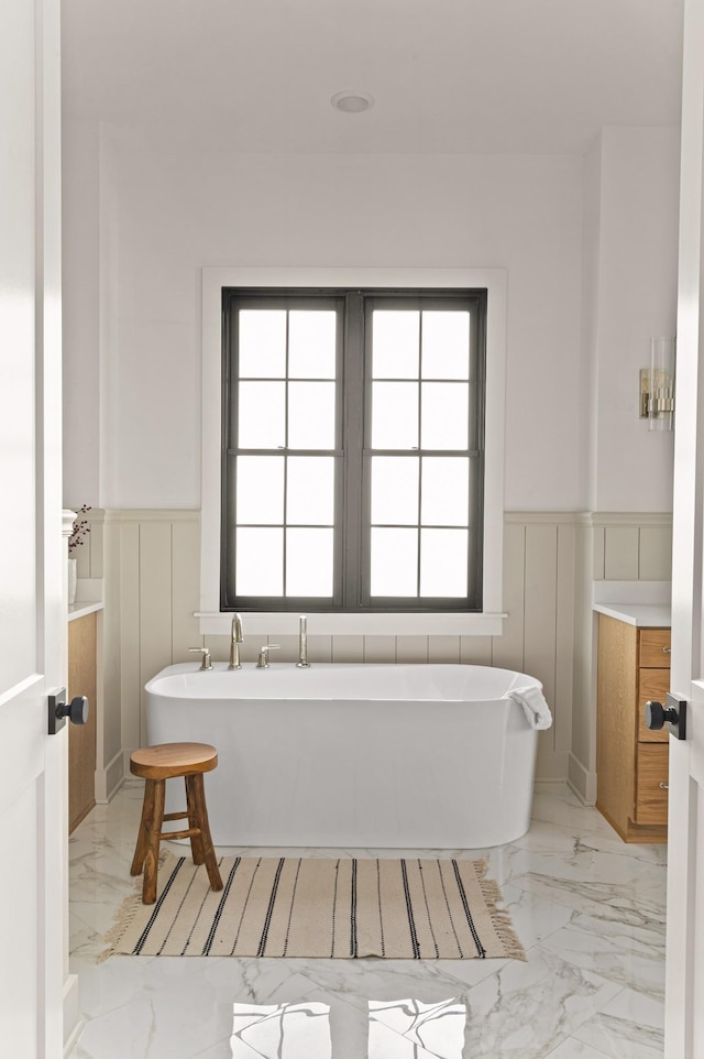 full bath featuring marble finish floor, wainscoting, and a soaking tub