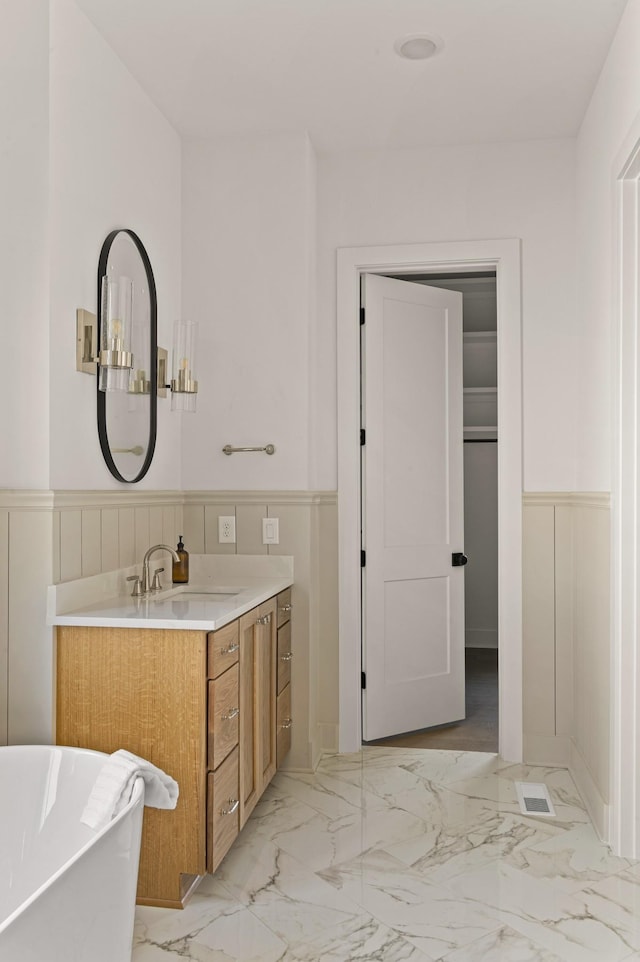 bathroom with marble finish floor, a wainscoted wall, a soaking tub, and vanity