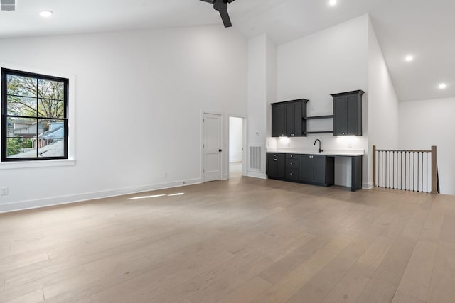 interior space featuring high vaulted ceiling, recessed lighting, a sink, baseboards, and light wood finished floors