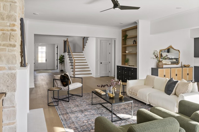 living room with ceiling fan, ornamental molding, stairway, and wood finished floors