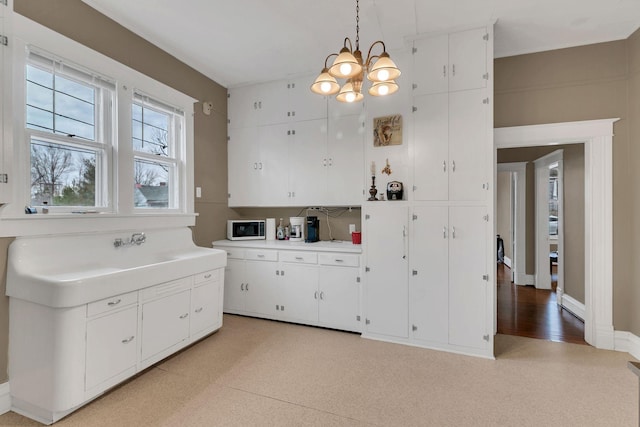 kitchen featuring decorative light fixtures, a chandelier, light floors, light countertops, and white cabinetry