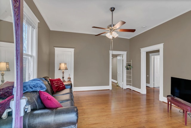 living area featuring baseboards, wood finished floors, a ceiling fan, and ornamental molding