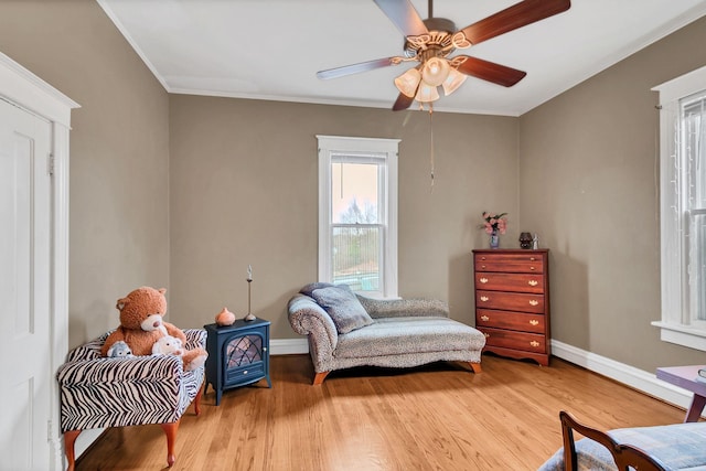 living area with baseboards, a ceiling fan, wood finished floors, and crown molding