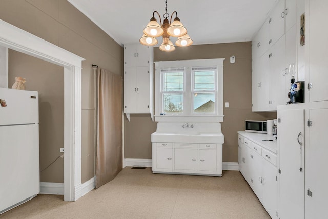 kitchen featuring baseboards, light countertops, a notable chandelier, white cabinets, and white appliances