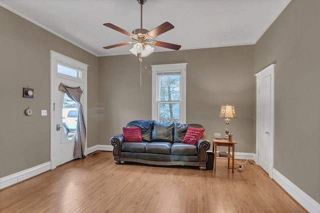 living room featuring ceiling fan, light wood-style floors, baseboards, and ornamental molding