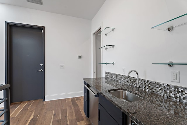 kitchen featuring dark wood-style flooring, a sink, visible vents, baseboards, and dark stone counters