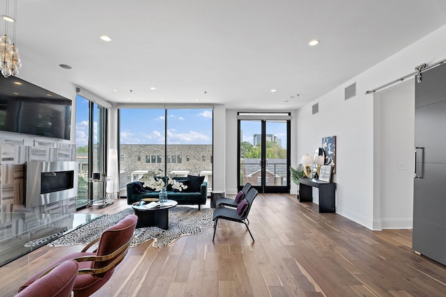 living area featuring floor to ceiling windows, visible vents, a barn door, wood finished floors, and baseboards