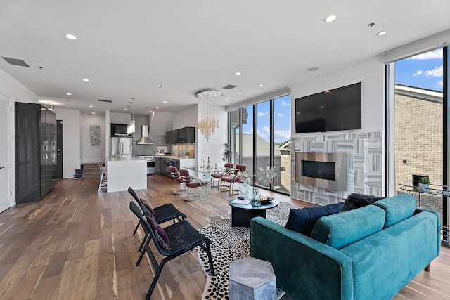 living room with recessed lighting, visible vents, a glass covered fireplace, expansive windows, and wood finished floors