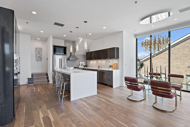 kitchen featuring modern cabinets, dark wood-style flooring, stainless steel appliances, light countertops, and wall chimney range hood