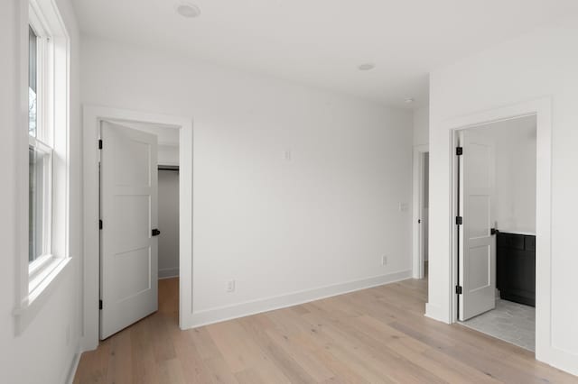 unfurnished bedroom featuring light wood-style flooring, baseboards, and a walk in closet