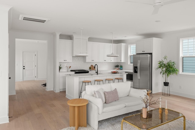 living room with light wood-style flooring, visible vents, ceiling fan, and baseboards