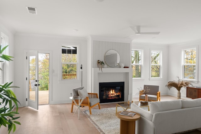 interior space with light wood finished floors, a large fireplace, baseboards, a ceiling fan, and ornamental molding