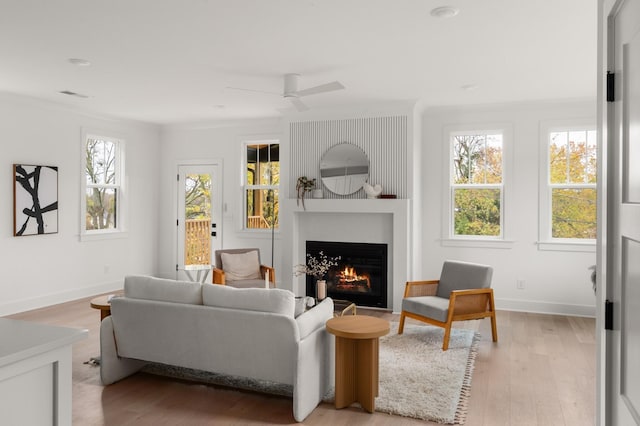 living room featuring ceiling fan, visible vents, baseboards, a lit fireplace, and light wood finished floors