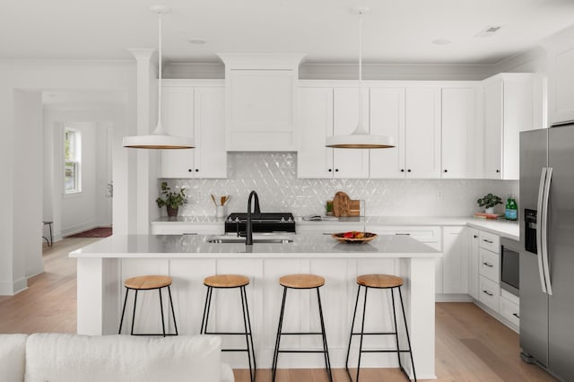 kitchen with a breakfast bar, white cabinetry, built in microwave, light wood finished floors, and stainless steel fridge