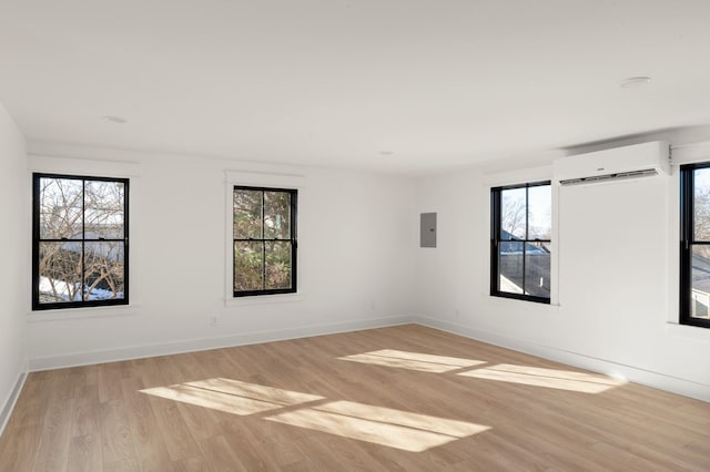 unfurnished room featuring light wood-style flooring, a wall unit AC, electric panel, and a healthy amount of sunlight