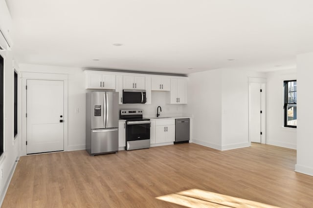 kitchen with appliances with stainless steel finishes, a sink, light wood-style flooring, and white cabinets