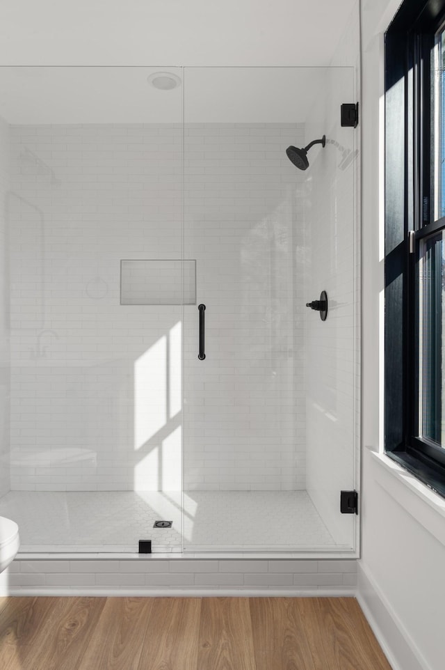 bathroom featuring toilet, a stall shower, baseboards, and wood finished floors