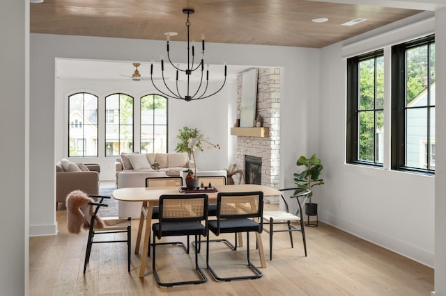 dining area featuring light wood-type flooring, a fireplace, an inviting chandelier, and baseboards