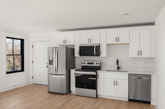 kitchen with stainless steel appliances, light countertops, white cabinetry, a sink, and light wood-type flooring