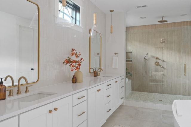 bathroom with double vanity, visible vents, a tile shower, and a sink