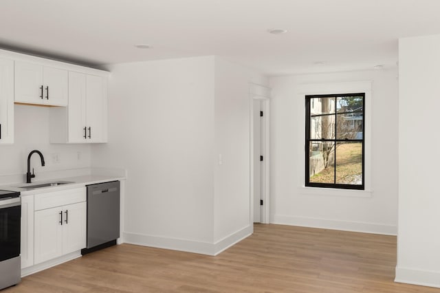 kitchen with stainless steel appliances, light countertops, light wood-style floors, a sink, and baseboards