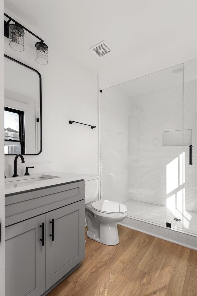 bathroom with a stall shower, visible vents, toilet, wood finished floors, and vanity