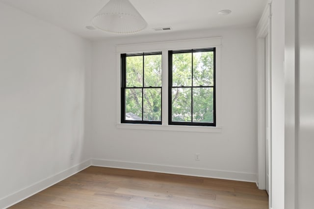 spare room featuring light wood-style floors, visible vents, and baseboards