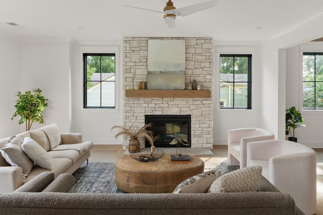 living area featuring a wealth of natural light, a stone fireplace, baseboards, and wood finished floors