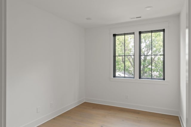 spare room with baseboards, light wood finished floors, visible vents, and a healthy amount of sunlight