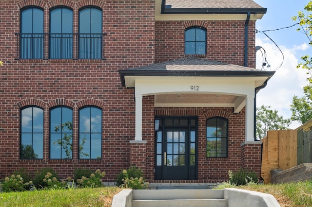 property entrance with roof with shingles and brick siding