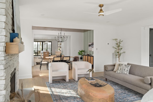 living area with a fireplace, ornamental molding, wood finished floors, baseboards, and ceiling fan with notable chandelier