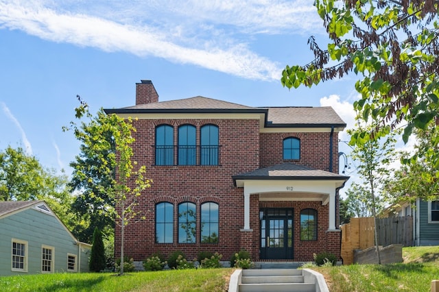 view of front of house with roof with shingles, brick siding, a chimney, and fence