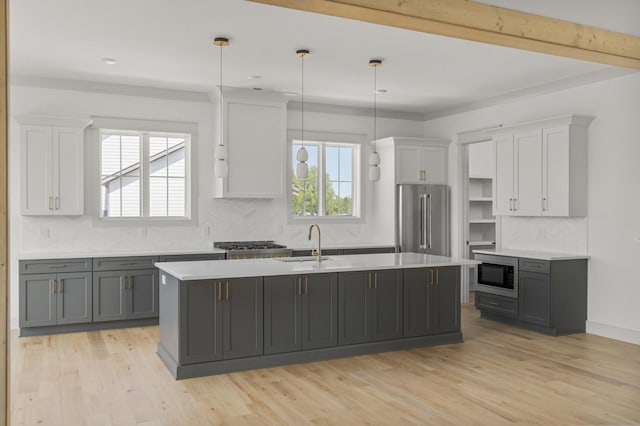 kitchen featuring an island with sink, high quality fridge, built in microwave, light countertops, and a sink