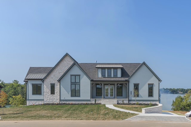 modern inspired farmhouse featuring metal roof, a water view, a standing seam roof, french doors, and a front yard