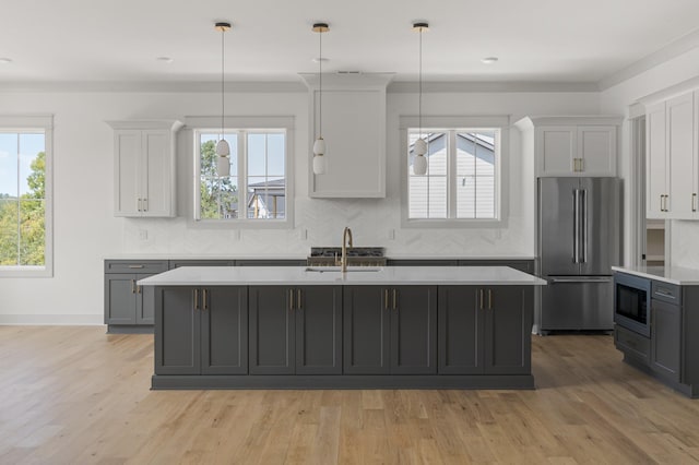 kitchen with light countertops, decorative backsplash, high quality fridge, a sink, and an island with sink