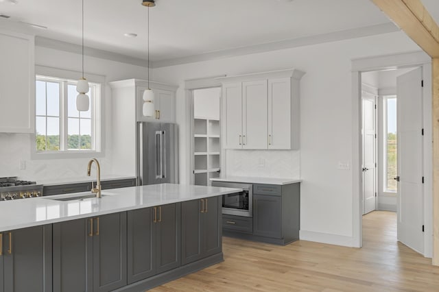 kitchen with light wood finished floors, stainless steel appliances, tasteful backsplash, light countertops, and a sink