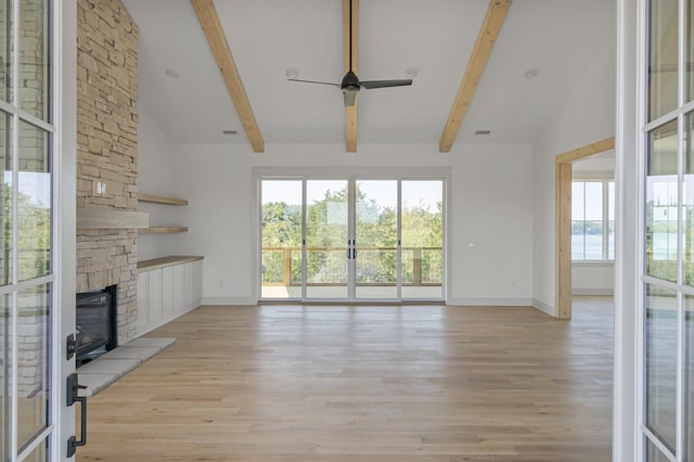 unfurnished living room featuring light wood-type flooring, a stone fireplace, and lofted ceiling with beams