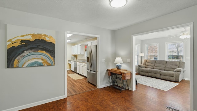 living room with a textured ceiling, dark wood-type flooring, visible vents, and baseboards