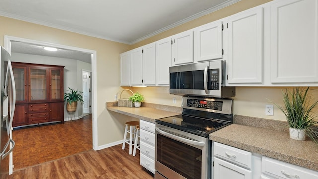 kitchen with appliances with stainless steel finishes, ornamental molding, wood finished floors, light countertops, and white cabinetry