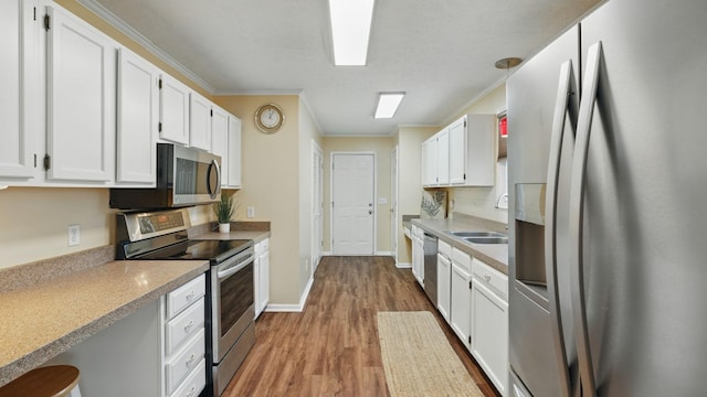 kitchen featuring stainless steel appliances, wood finished floors, a sink, white cabinets, and ornamental molding