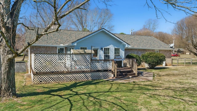 rear view of house with brick siding, a shingled roof, a lawn, fence, and a deck