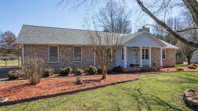 ranch-style home featuring brick siding, a chimney, a shingled roof, covered porch, and a front lawn