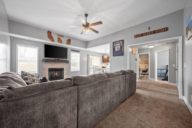 carpeted living room with plenty of natural light, baseboards, a ceiling fan, and a stone fireplace