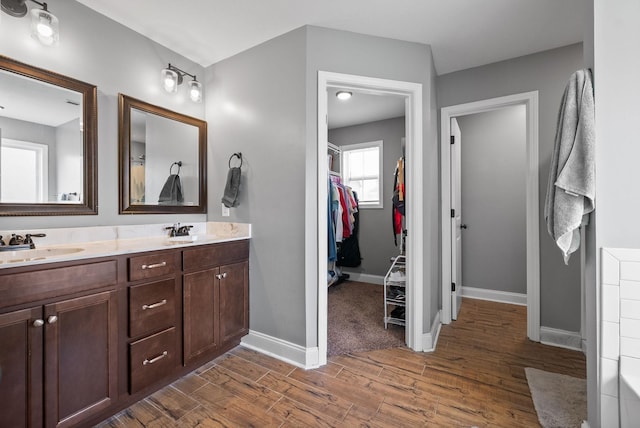 bathroom featuring double vanity, baseboards, wood finished floors, a walk in closet, and a sink