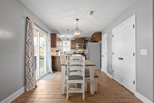 dining area featuring light wood-type flooring, visible vents, baseboards, and an inviting chandelier