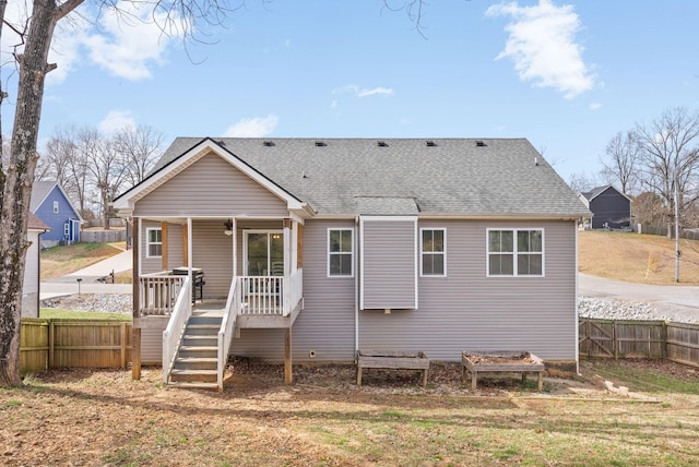 back of property with stairway, a shingled roof, and fence