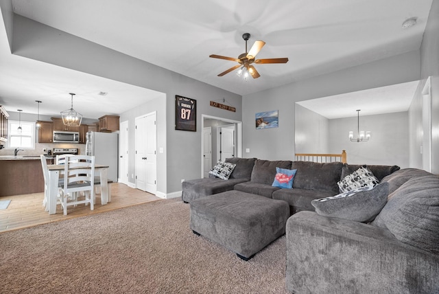 living room featuring light carpet, baseboards, and ceiling fan with notable chandelier